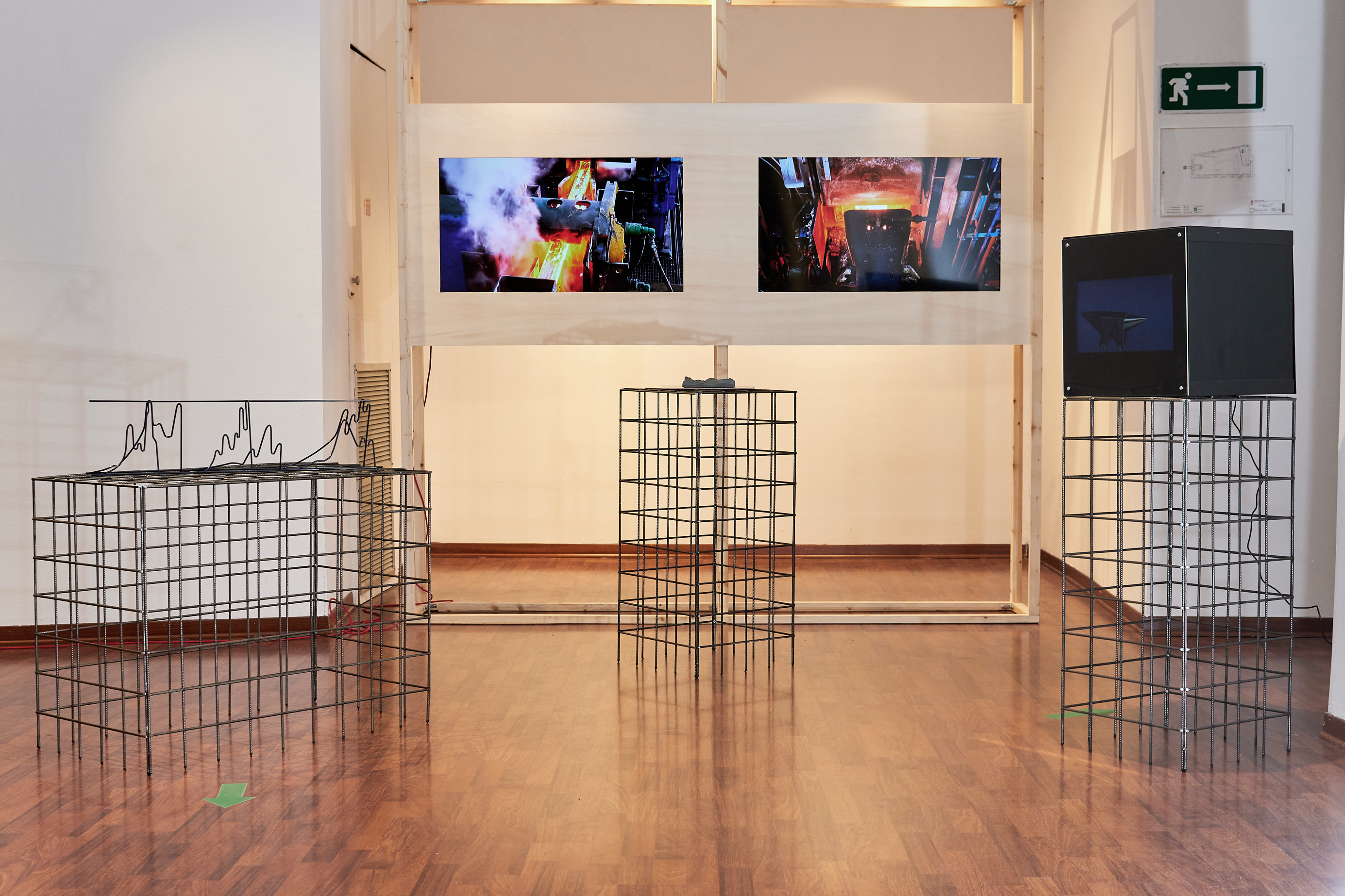 Installation view of La Rete <br/>Consisting of a two-screen video, 3D model animation, zinc coated 3D printed rendering of the Julian Alps and a re-imagined Pittini product. All objects sit on custom made wire mesh plinths made at the Pittini headquarters, Osoppo, Italy. <br/> <br/> "La Rete" is a dynamic and multifaceted work. It was born from the residence completed in Ferriere Nord Gruppo Pittini and narrates the resilient history of the company together with its deep bond with the territory. The various elements that make up the installation recall the company's production process, but also the suggestions that emerged in the exploration of the Udine foothills and Carnia, such as the 3D reproduction of the Predil quarries sprinkled with zinc dust or the reticular beam in which recreates the seismogram of the 1976 earthquake. The union of these elements symbolically generates a network of stories, people, work and knowledge.